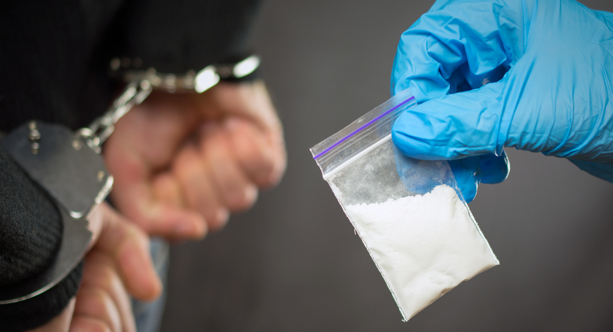 person in handcuffs with officer holding bag